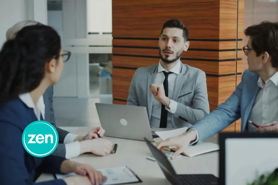 Business professionals discuss strategies in a modern conference room with laptops and documents.