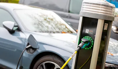 An electric car charges outdoors in cold weather from a grey charging station.