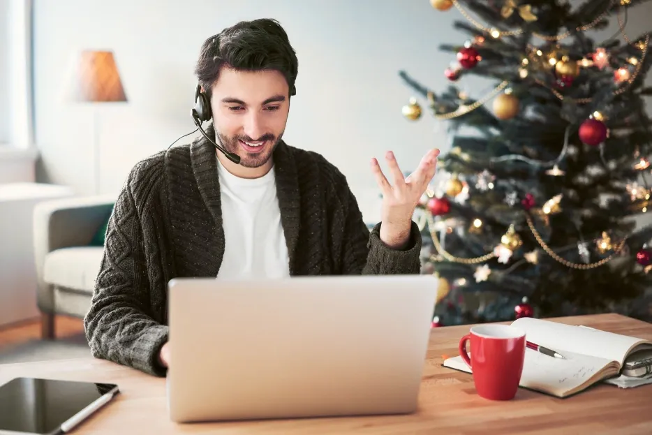 Man with headset on video call in home office with decorated Christmas tree.