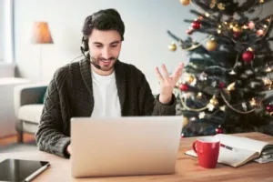 Man with headset having a video call on laptop with a Christmas tree in the background.