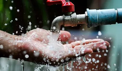Water gushes from a red-handled faucet onto cupped hands, splashing widely.