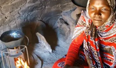 Woman in patterned headscarf cooking indoors on a small stove with a pot.