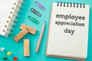 Notepad displaying 'employee appreciation day' text surrounded by office supplies on a turquoise surface.