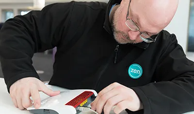 Man with glasses and beard in black jacket assembling electronic equipment on a white table.