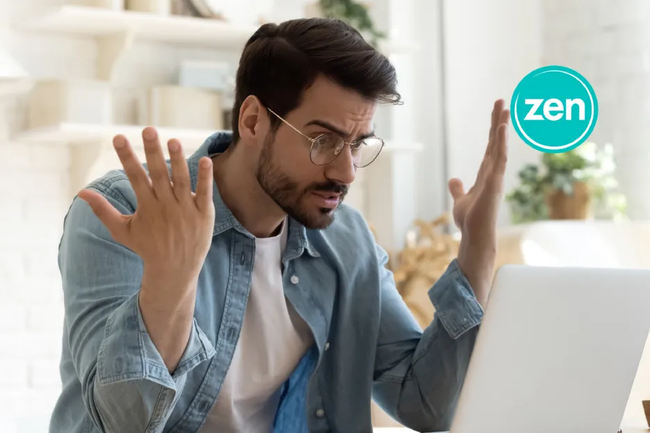 Frustrated man with glasses throws hands up while looking at his laptop screen.