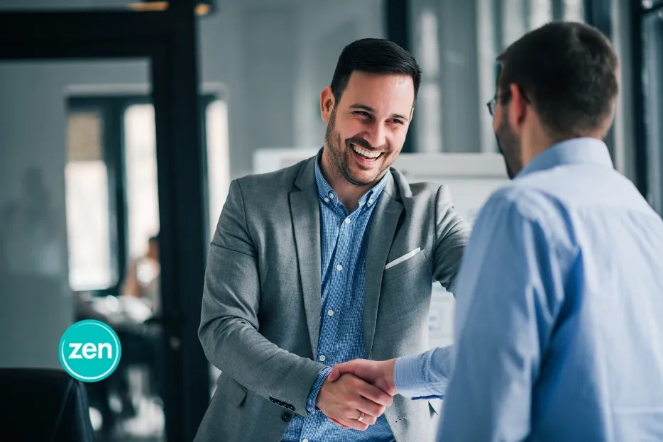 Two smiling businessmen shake hands in a modern office, completing a successful agreement.