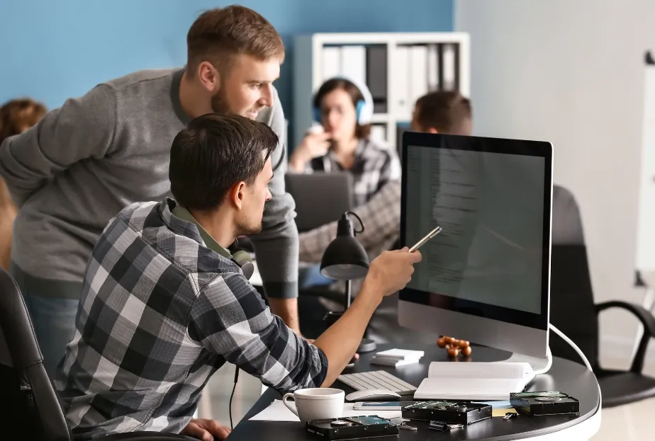 Two developers collaborate, reviewing code on a computer screen in an office.