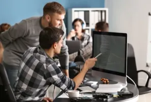 Two men collaborate, pointing at a computer screen in a modern office.