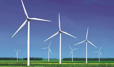 White wind turbines generate clean energy in a green field under a clear blue sky.