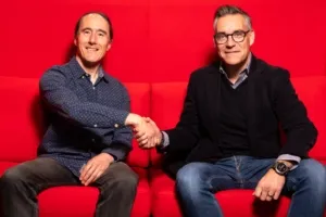 Two smiling men in casual attire shaking hands on a vibrant red background.