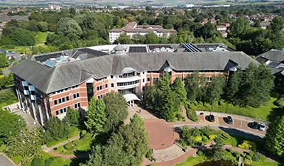 Large modern office building with a dark roof, brick facade, and lush green landscaping.