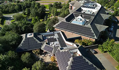 Aerial view of a building with many solar panels on its dark roofs.