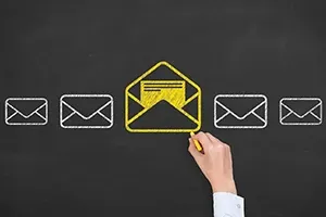 A hand draws a yellow open envelope among white closed envelopes on a chalkboard.