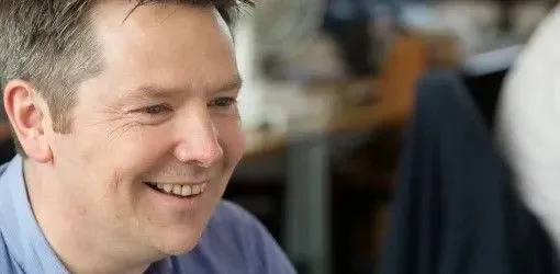 Smiling man with short dark hair in a blue shirt looks happily to the right.