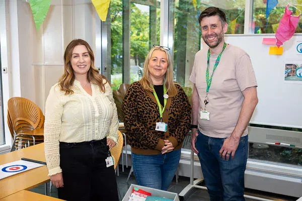 Three smiling educators stand in a decorated classroom, wearing lanyards.