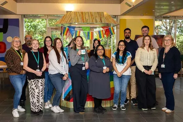 A diverse group of smiling people stands in front of a colorful, decorated booth at an event.