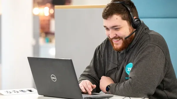 Bearded man in headphones smiling while working on a Dell laptop.