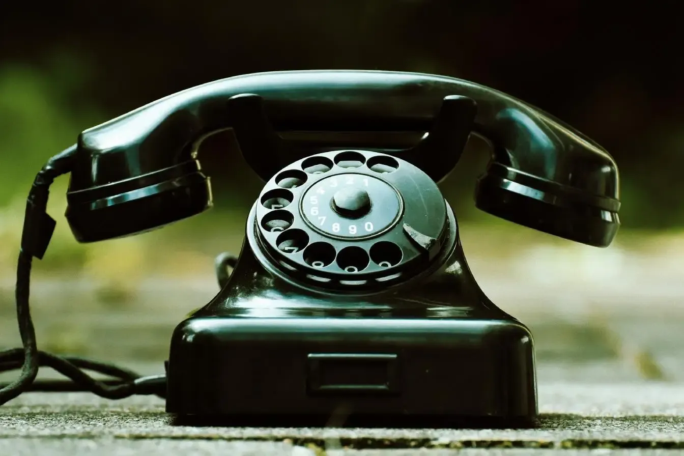 A vintage black rotary telephone with a classic design sits on a wooden surface.