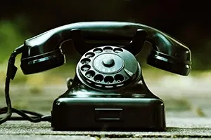 A shiny black vintage rotary telephone rests on a blurred outdoor surface.