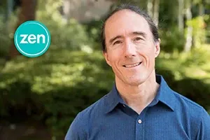 Smiling man in blue shirt with a zen logo. Green background.