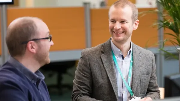 Two men, one smiling, conversing in a modern office environment.