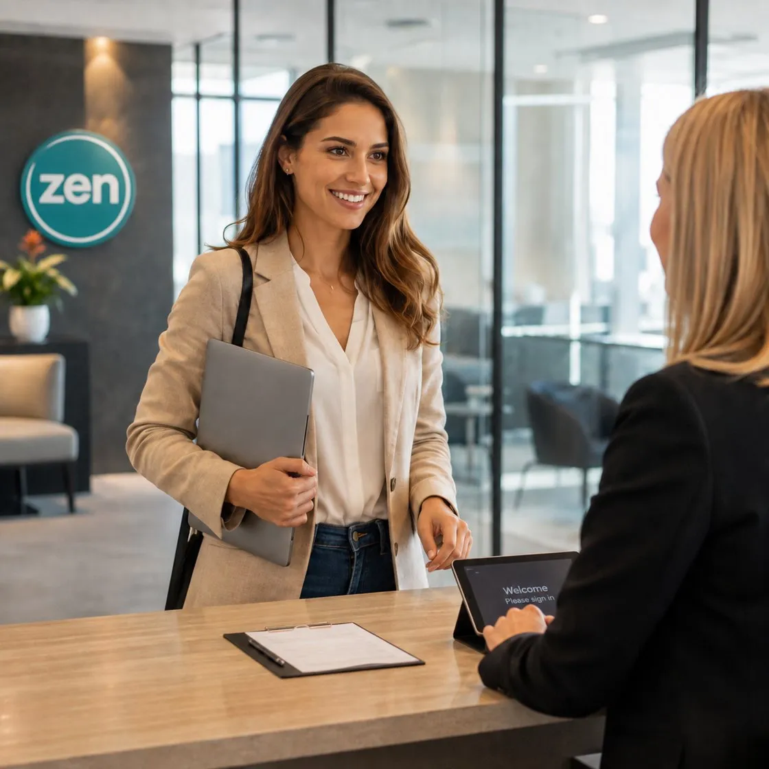 A smiling woman holding a laptop greets a receptionist at a modern office lobby.