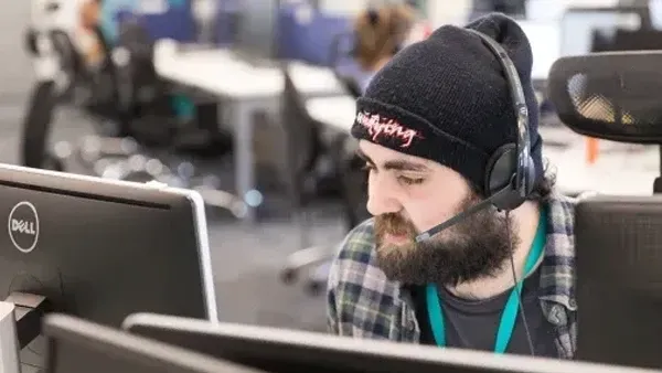 Man in beanie and headset intently looking at a computer screen in an office.