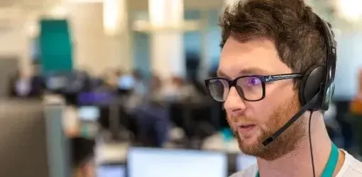 Man wearing glasses and headset speaks in an office environment.