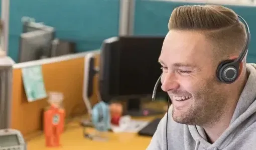 Man with a headset smiles while working in an office setting.